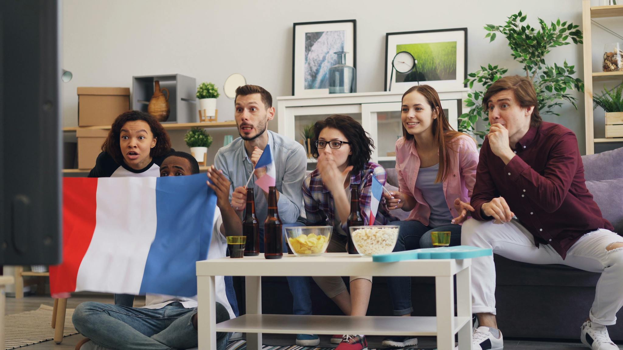 Friends excitedly watching a sports game indoors, supporting France with drinks and snacks.