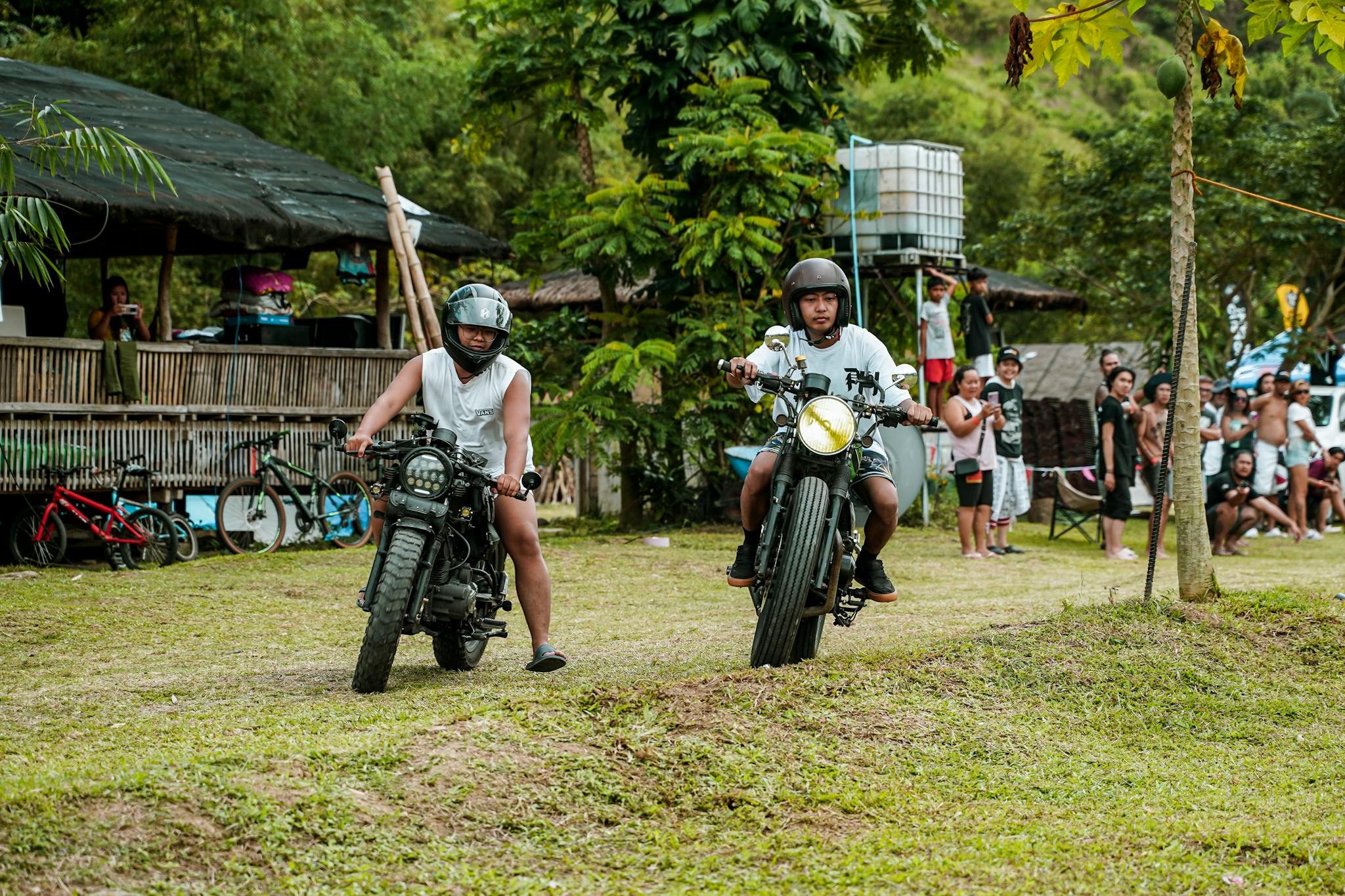 Two men on motorbikes in an outdoor event, surrounded by a lively crowd in Tanay, Philippines.